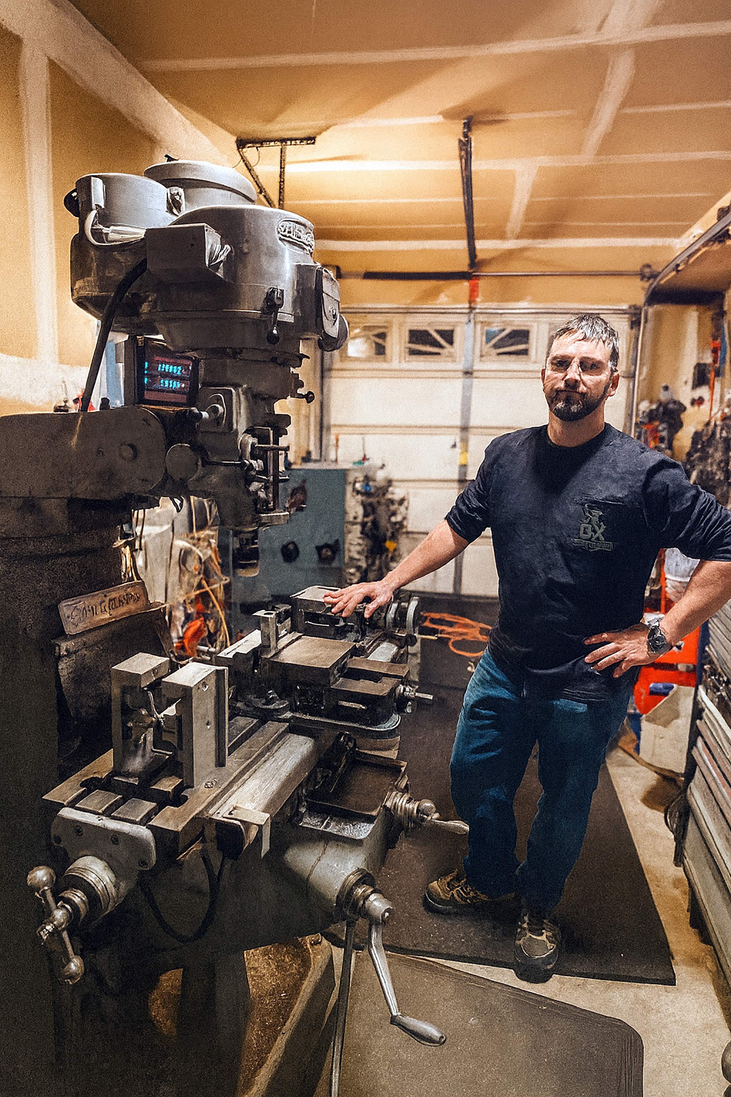 Wes Cranmore standing beside a manual milling machine inside the OX Bar Fabrication shop